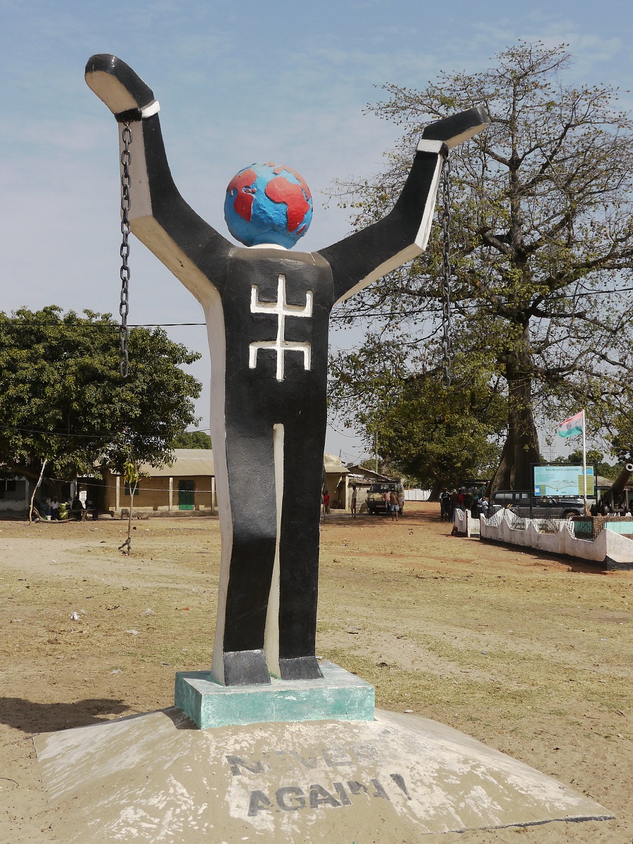 Statue of human figure with globe for the head and arms outstretched. An inscription at the base reads 'Never Again.'