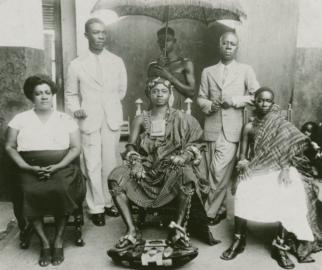 A group of African people gathered in a pose wearing traditional African and European clothing
